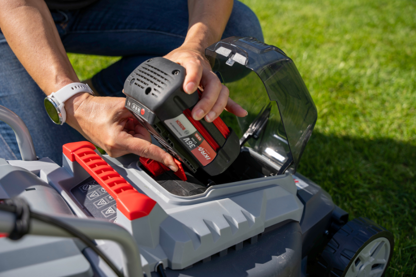 Nahaufnahme zeigt, wie ein 36 Volt BOSCH Akku in einen BOSCH Akku Rasenmäher eingesetzt wird.